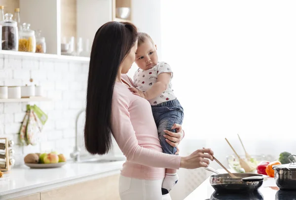 Junge Frau kocht mit Baby in Küche — Stockfoto