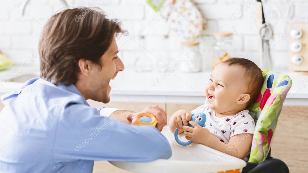 Millennial man laughing with his baby son in kitchen