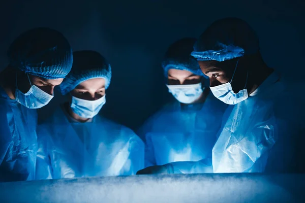 Equipo médico realizando operación quirúrgica en sala oscura — Foto de Stock