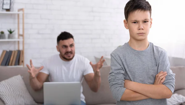 Trauriger kleiner Junge blickt in die Kamera, wütender Vater mit Laptop brüllt ihn an — Stockfoto
