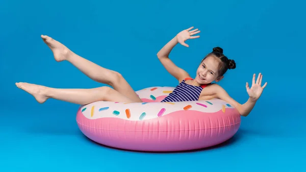 Счастливая маленькая девочка плавает на пончиковом розовом надувном кольце — стоковое фото