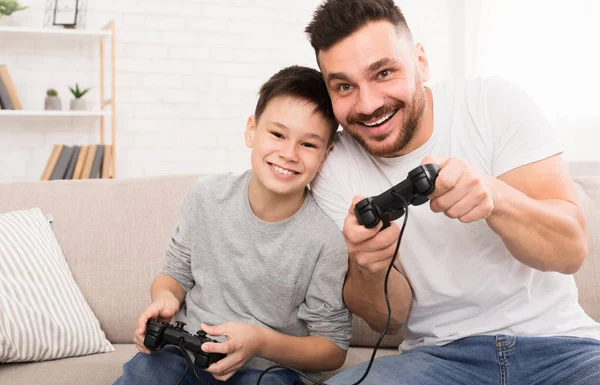 Niño feliz disfrutando de videojuegos con su papá, jugando con joysticks — Foto de Stock