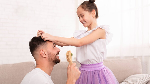 Little girl playing into hairdresser with her cheerful dad