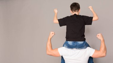 Oğlunu omuzlarında tutan kaslı adam, her ikisi de pazı lar gösteriyor.