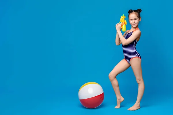 Little girl in swimsuit playing with water gun and inflatable beach ball — Stock Photo, Image