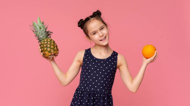 Pembe taze ananas ve portakal meyve tutan neşeli küçük kız