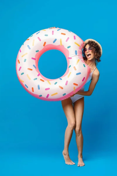 Menina negra engraçada em maiô mordendo anel de natação em forma de donut — Fotografia de Stock