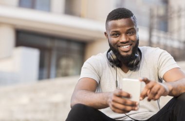 Genç Afro-Amerikalı adam dışarıda telefonuyla oturuyor.