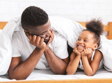 Sevimli Afrikalı baba ve kızı yatakta yatan ve birbirlerine gülümseyen
