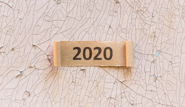 2020 text on torned curly sheet of brown paper on old wall — Stock Photo, Image