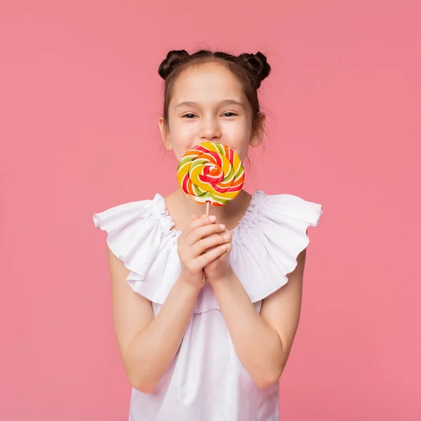 Linda niña disfrutando de dulces, cubriendo la boca con una gran piruleta colorida — Foto de Stock