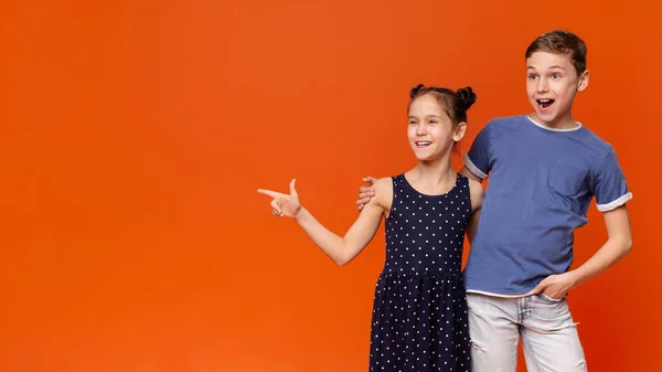 Staunende Kinder zeigen zur Seite auf leeren Raum, orangefarbenen Hintergrund — Stockfoto