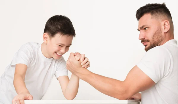 Сильный мальчик пытается победить, соревнуясь с отцом в армрестлинге — стоковое фото