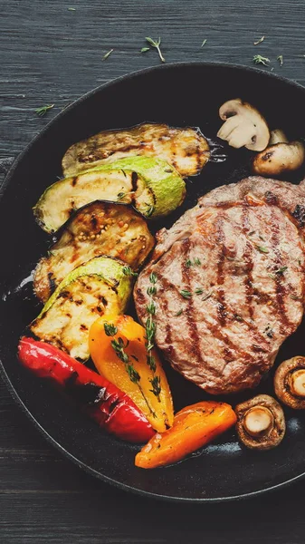 Grilled beef steak and roasted vegetables on dark wooden table — Stock Photo, Image