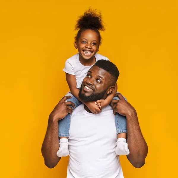 Fröhlicher schwarzer Mann reitet seine süße kleine Tochter auf Schultern — Stockfoto