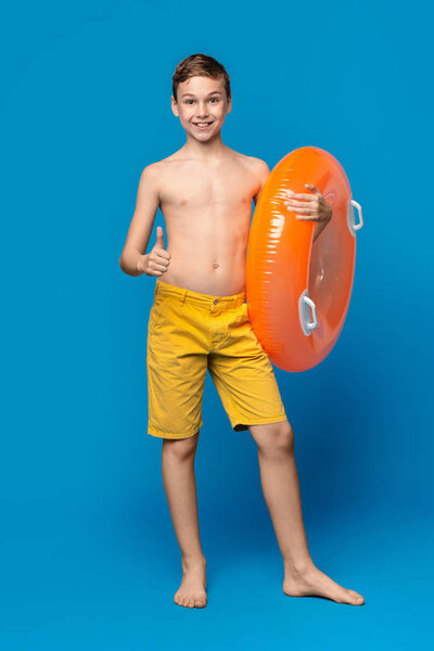 Cute boy in swimwear showing thumb up, holding orange inflatable ring
