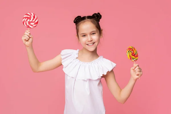 두 개의 큰 화려한 막대 사탕으로 미소 짓는 쾌활한 어린 소녀 — 스톡 사진