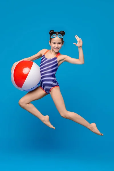 Little girl jumping with big inflatable ball, blue background — Stock Photo, Image