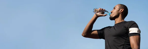 Afro Man bebiendo agua después de correr sobre fondo azul del cielo —  Fotos de Stock