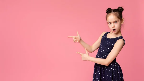 Menina legal apontando para o espaço vazio no fundo panorama rosa — Fotografia de Stock