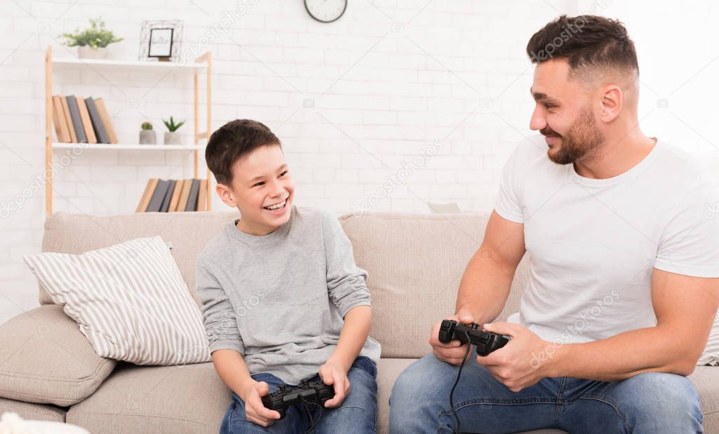 Cheerful father and son playing video game at home