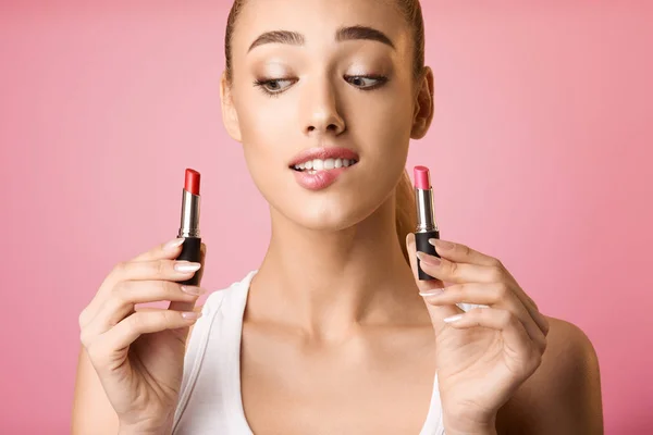 Verwirrtes Mädchen wählt zwischen zwei Lippenstiftfarben — Stockfoto