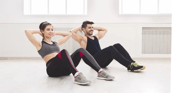 Pareja joven haciendo ejercicios deportivos en el suelo en estudio blanco — Foto de Stock