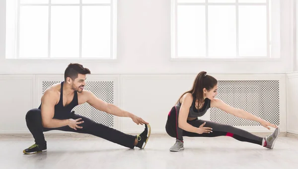 Sporty couple stretching legs before training in studio — Stock Photo, Image