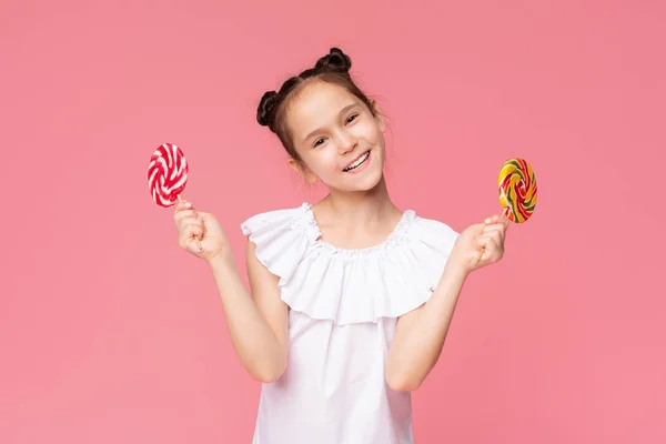 Adorável menina gostando de doce, segurando dois grandes pirulitos coloridos — Fotografia de Stock