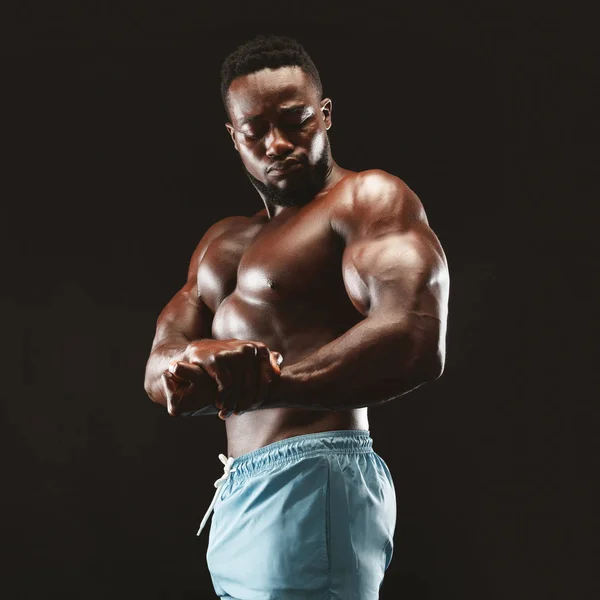 African kulturysta pokazując biceps w czarnym studiu — Zdjęcie stockowe