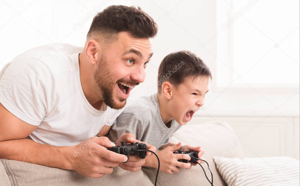 Emotional dad and son playing video game at home, competing for win