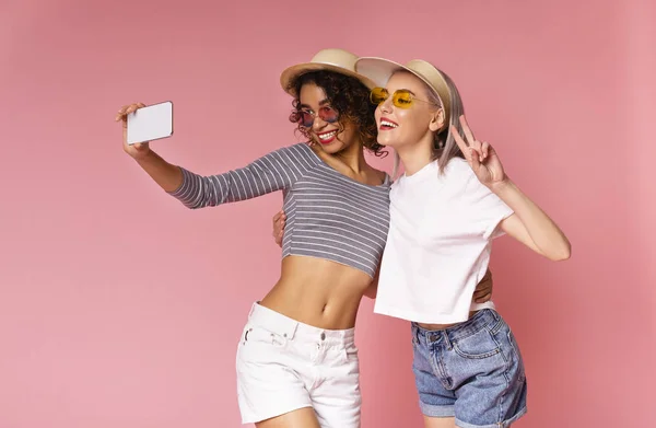 Две веселые молодые разноплановые женщины делают селфи на смартфоне — стоковое фото