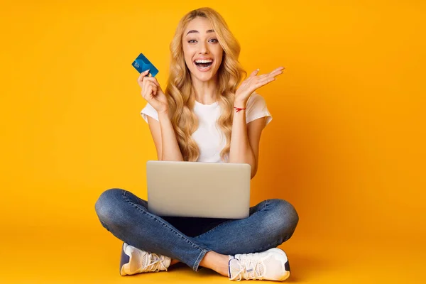 Mujer sorprendida sentada con computadora portátil y tarjeta de crédito —  Fotos de Stock