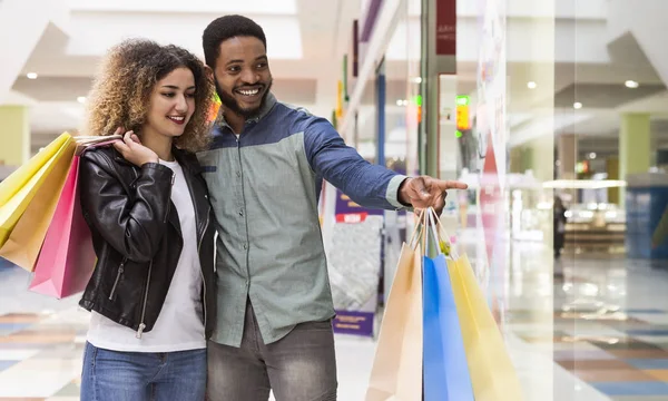 Young african guy pointing with finger at shopping window — Stock Photo, Image