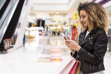 Cep telefonu kullanarak alışveriş torbaları ile kıvırcık saçlı Afrikalı kız