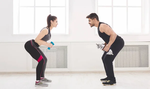 Deportiva pareja haciendo ejercicio con mancuernas en frente de la otra — Foto de Stock