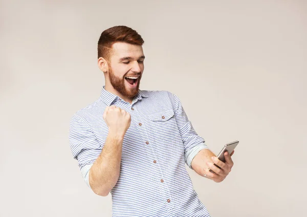 Freudiger Mann zeigt Ja-Zeichen und schaut auf sein Handy — Stockfoto