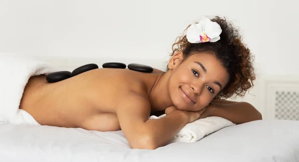 Relajado afro chica disfrutando de masaje de piedra caliente en el salón de spa — Foto de Stock