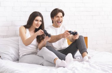Duygusal milenyumlar video oyunu oynarken, yatakta joystick ile oturuyor