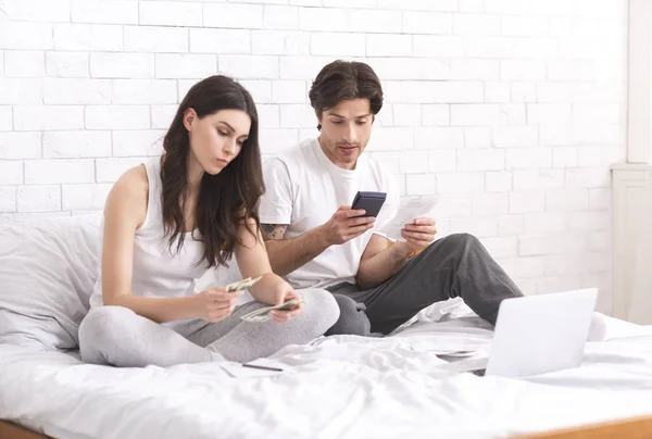 Молода пара сидить на ліжку вдома і перевіряє фінанси — стокове фото