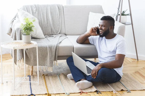 Αφρικανός Αμερικανός άνθρωπος μιλάει στο τηλέφωνο, δουλεύοντας με το laptop στο πάτωμα — Φωτογραφία Αρχείου