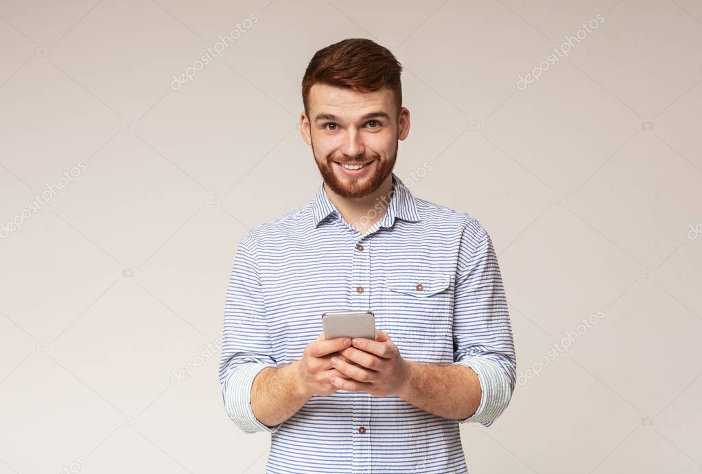 Young bearded man using his phone and smiling