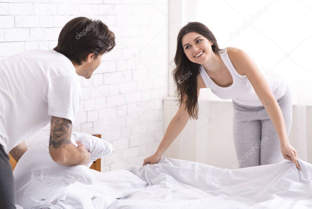 Sweet newlyweds making bed together in morning