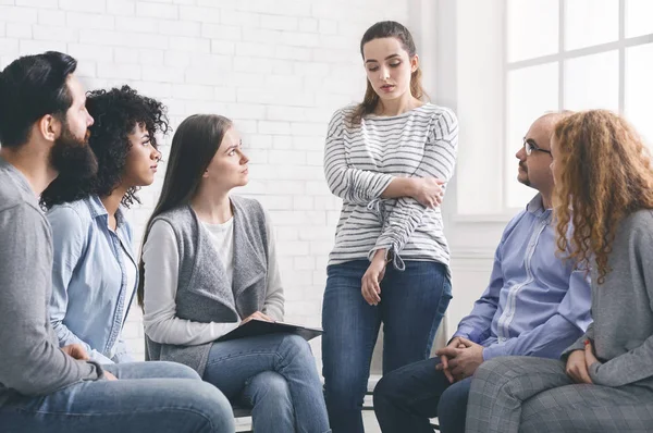 Sad addicted woman sharing her problems at rehab group meeting