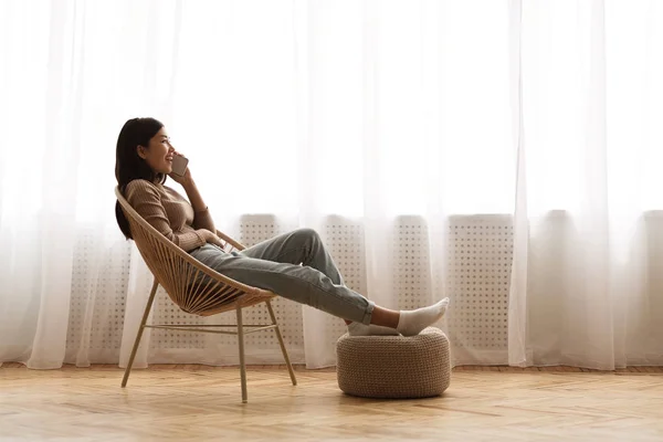 Entspanntes Mädchen telefoniert am Fenster, sitzt auf Stuhl — Stockfoto