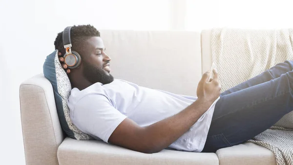 Afrikansk kille njuter film på mobiltelefon, vilar hemma — Stockfoto