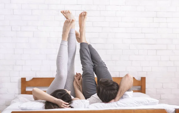 年轻夫妇躺在床上，在空中抬起双腿 — 图库照片