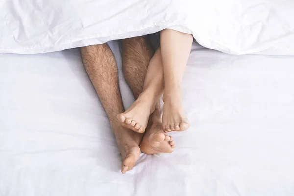 Мужские и женские ноги под одеялом лежат на кровати — стоковое фото