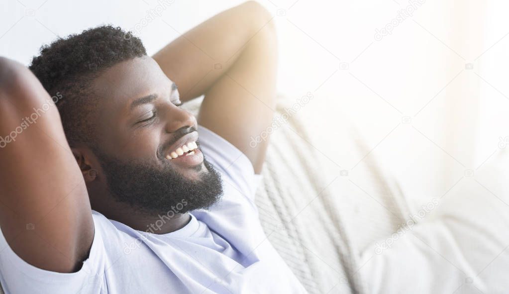 Satisfied black guy relaxing at home, lying with closed eyes