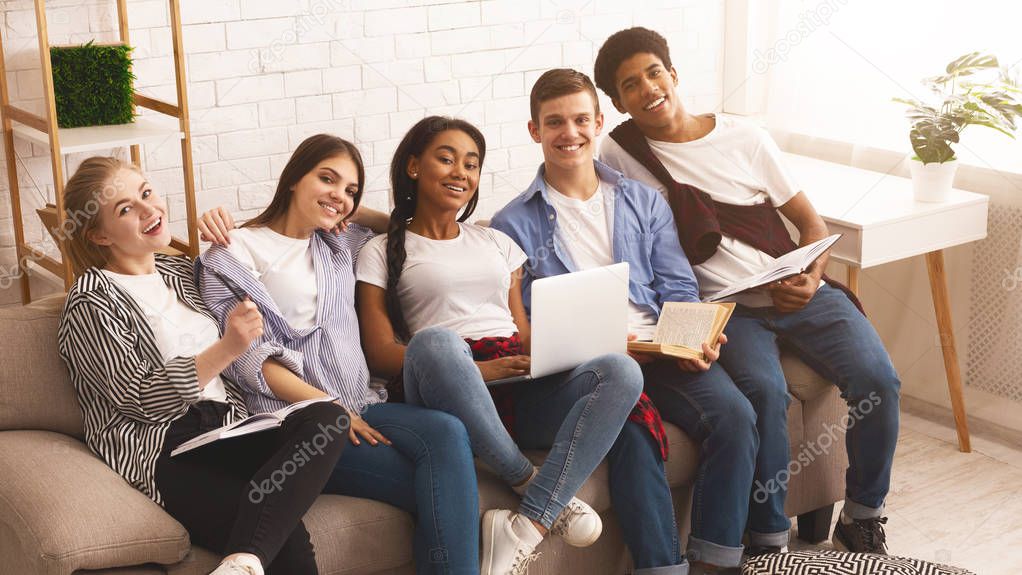 Diverse students with laptop and books in home interior